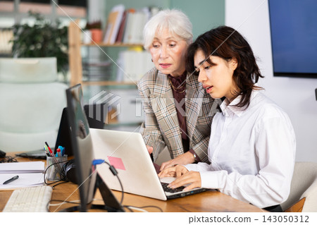 Elderly woman helping young woman with laptop Elderly woman helping young woman with laptop 143050312