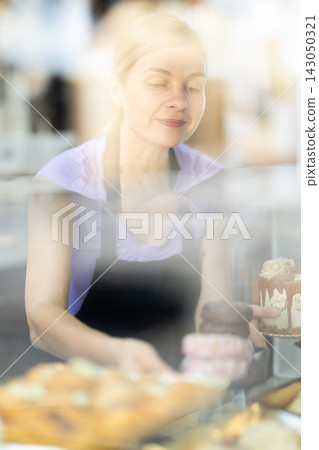 Young woman seller stands at bakery counter, present croissant Young woman seller stands at bakery counter, present croissant 143050321