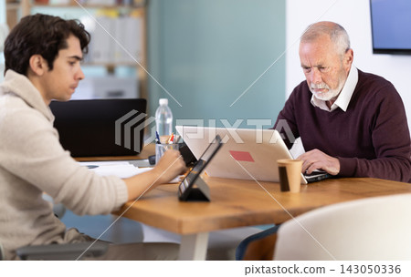 Two male manager work on laptops in modern company office Two male manager work on laptops in modern company office 143050336