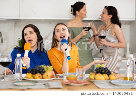 Group of female friends having fun at alcoholic bachelorette party in cozy living room, drinking red wine and singing together at home karaoke Group of female friends having fun at alcoholic bachelorette party in cozy living room, drinking red wine and singing together at home karaoke 143050481