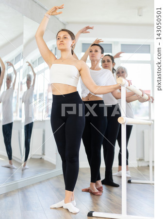 Female ballet dancers doing various ballet movements at ballet barre in fifth position Female ballet dancers doing various ballet movements at ballet barre in fifth position 143050501