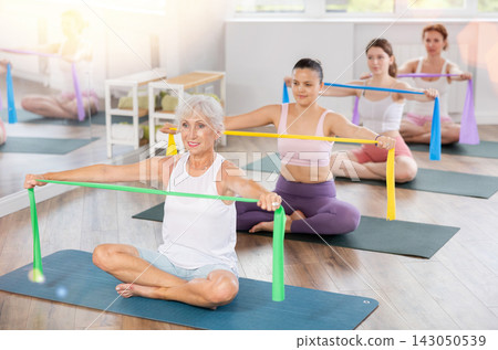 Senior lady performing exercises with resistance band in pilates class Senior lady performing exercises with resistance band in pilates class 143050539