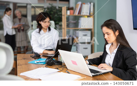 Young woman works on laptop with female colleagues Young woman works on laptop with female colleagues 143050671