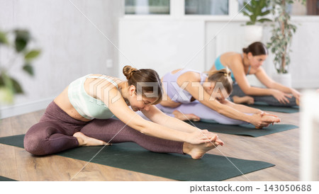 Active women perform a stretching exercise in a pose Janu Shirshasana Active women perform a stretching exercise in a pose Janu Shirshasana 143050688