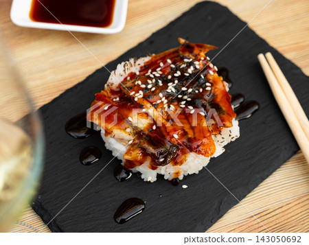Japanese appetizer with fried eel, saucer and rice on a stone stand with chopsticks Japanese appetizer with fried eel, saucer and rice on a stone stand with chopsticks 143050692