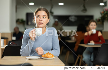 Young girl enjoying coffee and croissant in cafeteria 143050701