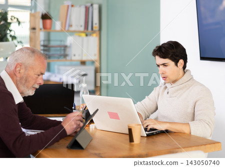 Elderly man working on tablet and young man on laptop in office 143050740