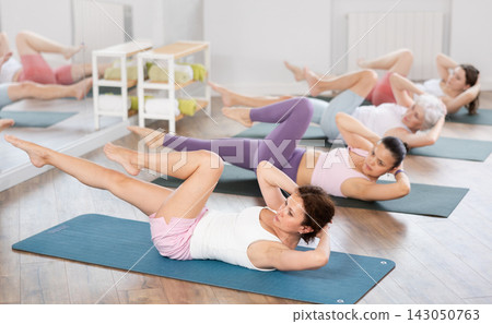 Athletic women doing pilates or aerobics - doing back exercises during group training in gym Athletic women doing pilates or aerobics - doing back exercises during group training in gym 143050763