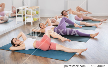 Athletic women doing pilates or aerobics - doing back exercises during group training in gym Athletic women doing pilates or aerobics - doing back exercises during group training in gym 143050804