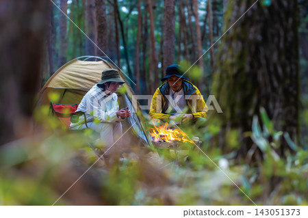 一對男女在森林露營地的營火旁享用咖啡。 一對男女在森林露營地的營火旁享用咖啡。 143051373