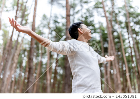 森林中,一個男人張開雙臂,仰望天空。 森林中,一個男人張開雙臂,仰望天空。 143051381