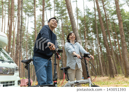 一對笑容滿面的夫婦在森林裡騎著折疊自行車。 一對笑容滿面的夫婦在森林裡騎著折疊自行車。 143051393