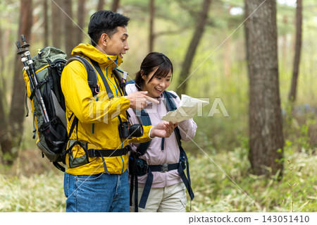 一男一女在森林裡健行,一邊查看地圖一邊互相商量。 一男一女在森林裡健行,一邊查看地圖一邊互相商量。 143051410