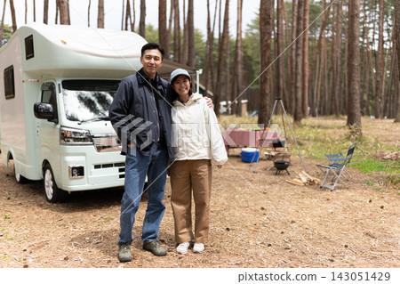 一對夫婦把車停在森林露營地的一輛露營車旁。 一對夫婦把車停在森林露營地的一輛露營車旁。 143051429
