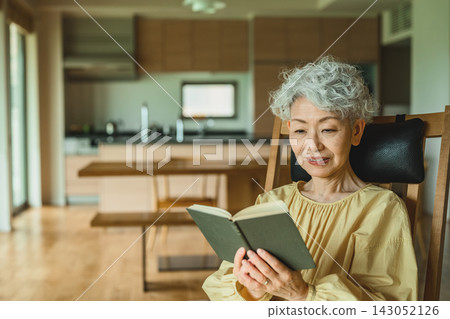 一位老婦人坐在椅子上看書。 一位老婦人坐在椅子上看書。 143052126
