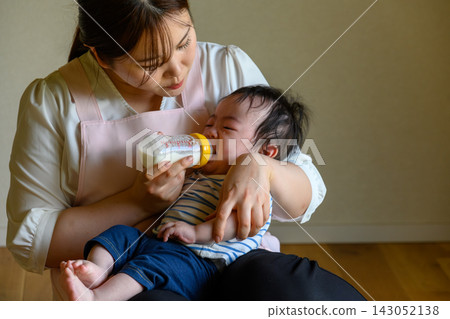 A mother feeding her crying baby milk from a bottle. A mother feeding her crying baby milk from a bottle. 143052138