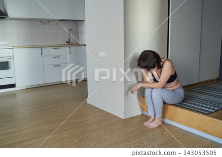 Adult Woman Crouched On Step Near Open Kitchen Wall In Compact Apartment Wearing Workout Clothes Adult Woman Crouched On Step Near Open Kitchen Wall In Compact Apartment Wearing Workout Clothes 143053505