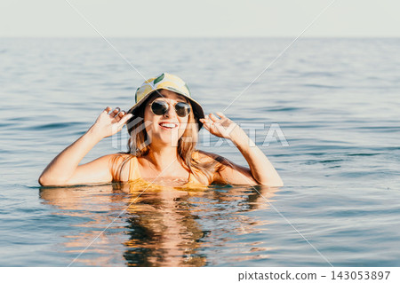 Woman Sunglasses Ocean - Smiling woman wearing sunglasses and a hat floats in the ocean on a sunny day. Woman Sunglasses Ocean - Smiling woman wearing sunglasses and a hat floats in the ocean on a sunny day. 143053897