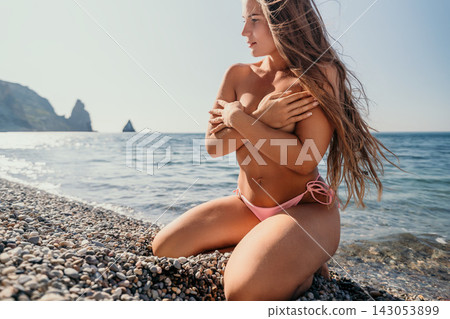 Woman beach bikini sitting on a pebbled coast by the blue ocean during a bright summer day with clear sky Woman beach bikini sitting on a pebbled coast by the blue ocean during a bright summer day with clear sky 143053899