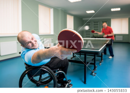 Adult disabled man in a wheelchair play at table tennis with his coach Adult disabled man in a wheelchair play at table tennis with his coach 143055833