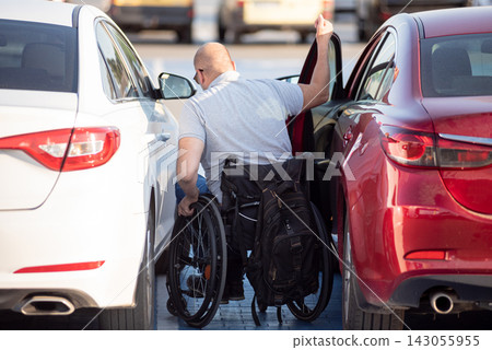 Young handicapped driver getting in red car fom wheelchair 143055955