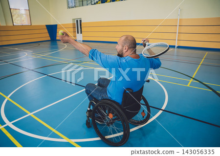 Adult man with a physical disability in a wheelchair playing tennis on indoor tennis court 143056335