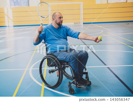 Adult man with a physical disability in a wheelchair playing tennis on indoor tennis court Adult man with a physical disability in a wheelchair playing tennis on indoor tennis court 143056347
