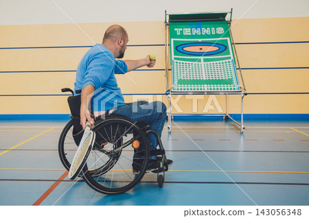 Adult man with a physical disability in a wheelchair playing tennis on indoor tennis court Adult man with a physical disability in a wheelchair playing tennis on indoor tennis court 143056348