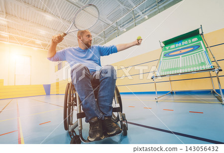 Adult man with a physical disability in a wheelchair playing tennis on indoor tennis court Adult man with a physical disability in a wheelchair playing tennis on indoor tennis court 143056432