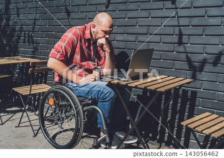 Freelancer with a physical disability in a wheelchair working at the street cafe Freelancer with a physical disability in a wheelchair working at the street cafe 143056462