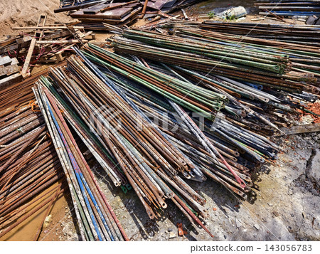 Rusted steel rebar rods stacked outdoors at construction site with dusty ground 143056783