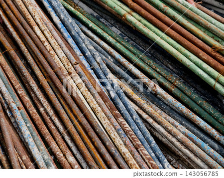 Rusted steel rebar rods stacked outdoors at construction site with dusty ground 143056785