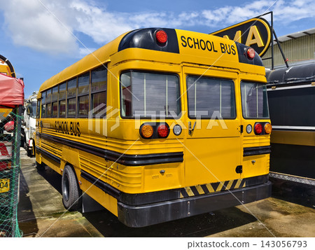 Yellow school bus parked outdoors on paved lot beside other buses Yellow school bus parked outdoors on paved lot beside other buses 143056793
