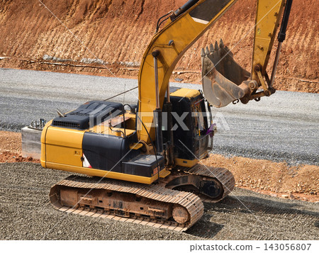 Yellow excavator compacting gravel beside roadside earthworks at construction site Yellow excavator compacting gravel beside roadside earthworks at construction site 143056807