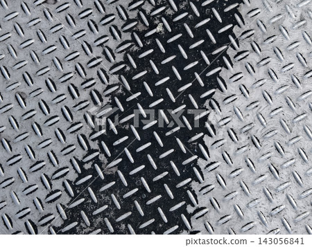 Diagonal shadow across textured metal diamond plate with alternating light and dark bands 143056841
