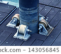 Rusty metal pipe support with three roller wheels on weathered wooden deck in sunlight 143056845