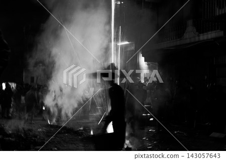 Silhouetted figure amid fireworks sparks and smoke on a dark street at night Silhouetted figure amid fireworks sparks and smoke on a dark street at night 143057643