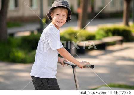 Boy in a hat riding a scooter and having fun Boy in a hat riding a scooter and having fun 143057750