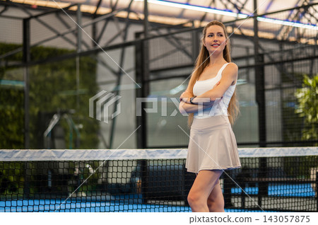 Pretty long-haired woman in a tennis skirt standing at the paddle court 143057875