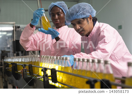 Asian male and black woman factory workers monitoring cold drink bottles on production line at drinks production plant. Asian male and black woman factory workers monitoring cold drink bottles on production line at drinks production plant. 143058173