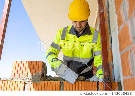 Focused bricklayer in hard hat smoothing cement mortar using steel trowel Focused bricklayer in hard hat smoothing cement mortar using steel trowel 143058428