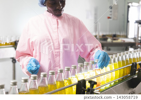 Black woman inspecting drink quality with rows of glass bottles on the automated conveyor system in manufacturing assembly line. Black woman inspecting drink quality with rows of glass bottles on the automated conveyor system in manufacturing assembly line. 143058719
