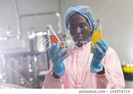 Black woman inspecting drink quality with rows of glass bottles on the automated conveyor system in manufacturing assembly line. Black woman inspecting drink quality with rows of glass bottles on the automated conveyor system in manufacturing assembly line. 143058729