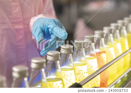 Black woman inspecting drink quality with rows of glass bottles on the automated conveyor system in manufacturing assembly line. Black woman inspecting drink quality with rows of glass bottles on the automated conveyor system in manufacturing assembly line. 143058733