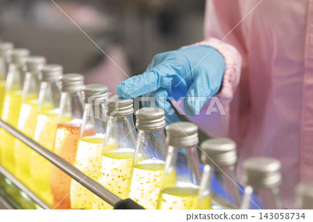 Black woman inspecting drink quality with rows of glass bottles on the automated conveyor system in manufacturing assembly line. 143058734