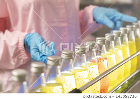 Black woman inspecting drink quality with rows of glass bottles on the automated conveyor system in manufacturing assembly line. Black woman inspecting drink quality with rows of glass bottles on the automated conveyor system in manufacturing assembly line. 143058736