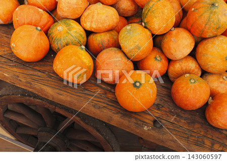 Small pumpkins piled in a wooden cart, highlighting a cozy, rustic seasonal atmosphere with warm autumn charm. Small pumpkins piled in a wooden cart, highlighting a cozy, rustic seasonal atmosphere with warm autumn charm. 143060597