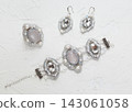 Handmade wedding jewelry set, luxury embroidered earrings, bracelet and ring with pearls, gems, crystals and seedbeads , lying flat on the white stone background, top view 143061058