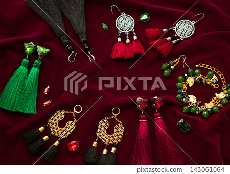 Handmade set of green,golden,black,silver and vinous bijouterie with gems, tassels, cryslals and beads, lying on the vinous velvet background, top flat view with empty place for your text Handmade set of green,golden,black,silver and vinous bijouterie with gems, tassels, cryslals and beads, lying on the vinous velvet background, top flat view with empty place for your text 143061064