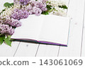Beautiful white and violet lilac flowers with opened note-book lying on the white wooden background, mock up perspective view 143061069